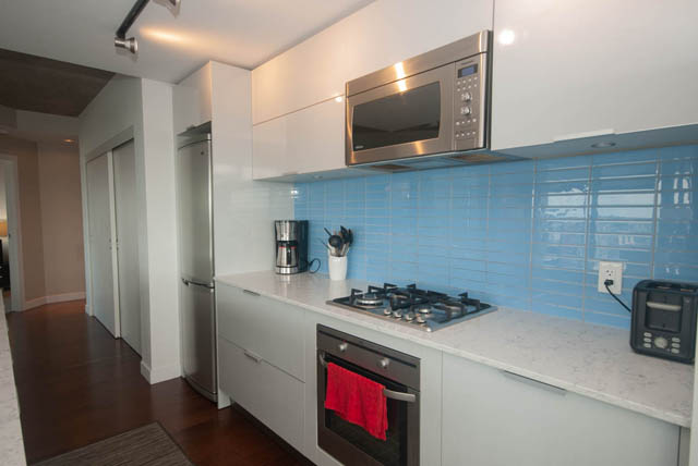 Bright kitchen with white cabinets, blue backsplash, stainless steel appliances, and hardwood floors. - 3806 - 128 Cordova St W, Vancouver Downtown