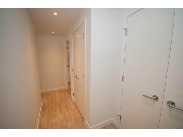 Bright hallway with wooden floors and white walls leading to a door. - 1108 - 1661 Quebec St, Vancouver West Side