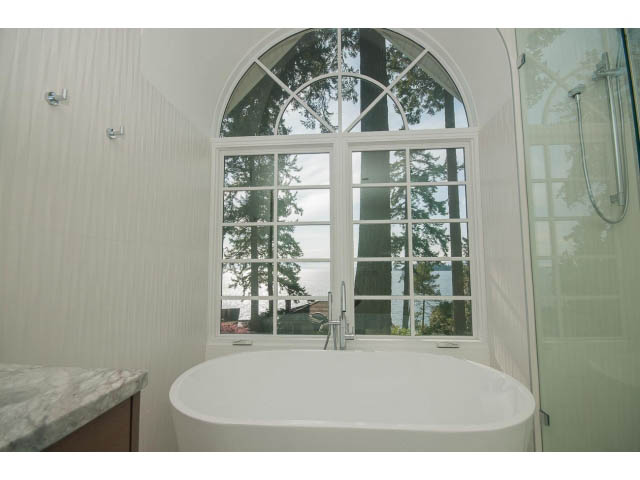 Bathroom with large arched window, view of trees and water, modern sink and shower. - 6018 Gleneagles Place, West Vancouver