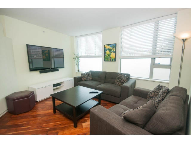 Furnished living room with hardwood floors, modern furniture, and large windows. - 202 - 1277 Nelson St, Vancouver Downtown