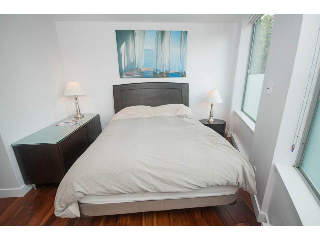 Bright bedroom with hardwood floors, large window, and modern artwork above the bed. - 202 - 1277 Nelson St, Vancouver Downtown