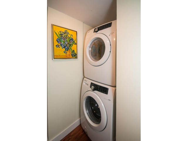 Bright laundry room with stacked washer and dryer, colorful floral artwork on the wall. - 202 - 1277 Nelson St, Vancouver Downtown