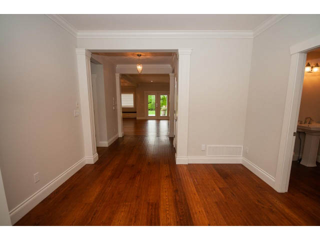 Bright living room with hardwood floors and white walls, leading to a kitchen area. - 3476 Wellington Crescent, North Vancouver