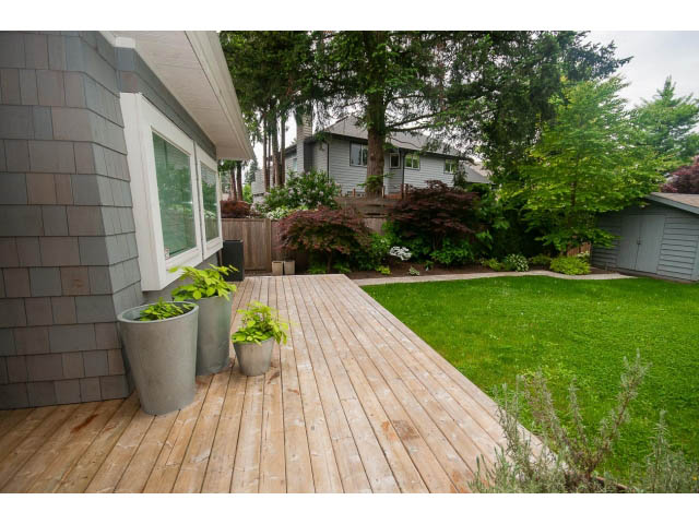 Furnished deck with wooden flooring and greenery, leading to a grassy yard. - 3476 Wellington Crescent, North Vancouver