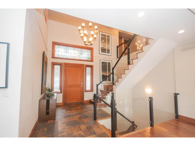 Staircase with glass railings leading to upper level, hardwood floors, and chandelier above. - Upper - 4407 Prospect Rd, North Vancouver