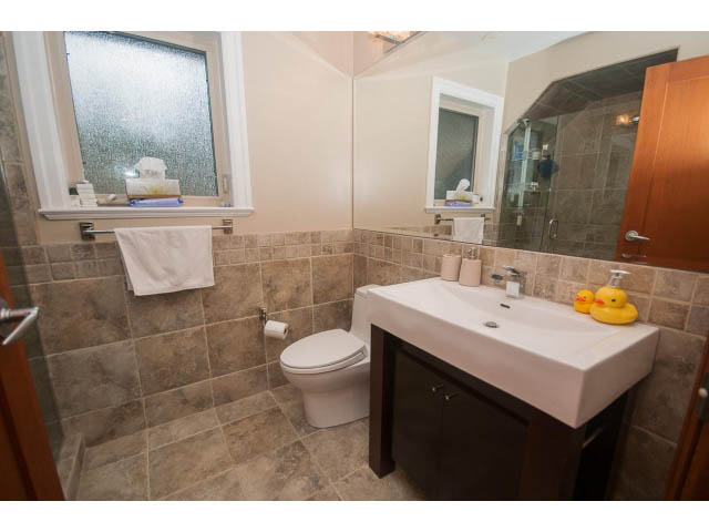 Modern bathroom with tiled walls, white sink, and frosted window. - Upper - 4407 Prospect Rd, North Vancouver