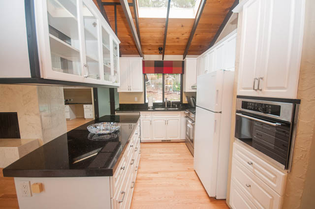 Bright kitchen with black countertops, white cabinets, and hardwood floors. - 4645 Caulfeild Drive, West Vancouver
