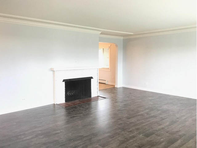 Bright living room with hardwood floors and a fireplace, leading to a kitchen area. - 618 7th Street East, North Vancouver