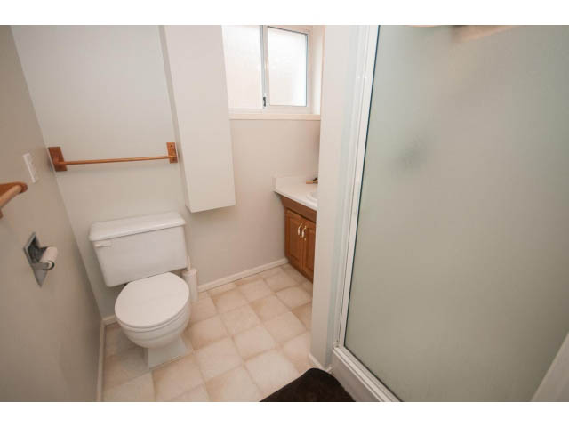 Bathroom with white fixtures, wooden cabinet, and frosted glass shower door. - 618 7th Street East, North Vancouver