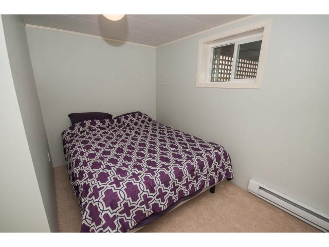 Furnished bedroom with purple patterned bedding and small window. - 618 7th Street East, North Vancouver