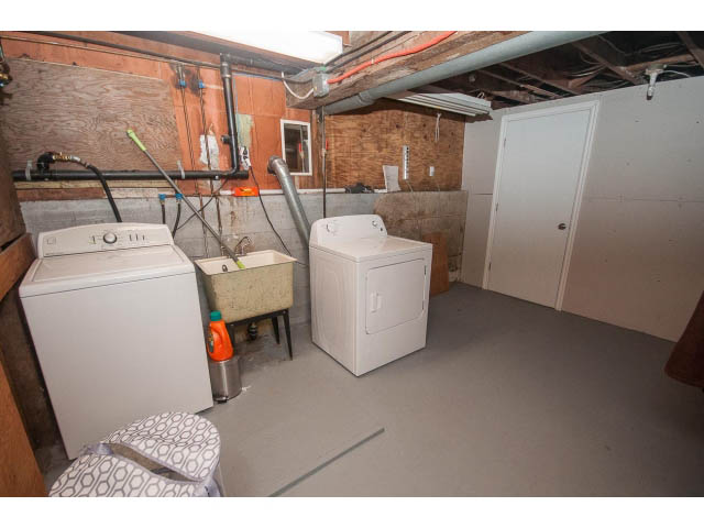 Laundry room with stacked washer and dryer, exposed pipes, and unfinished walls. - 618 7th Street East, North Vancouver