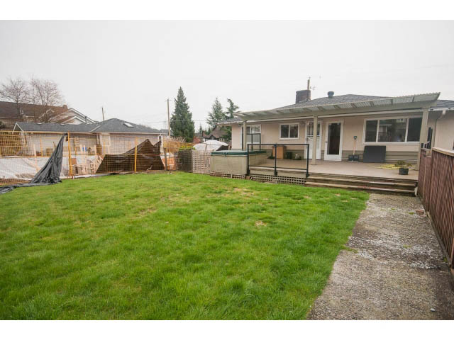 Lush green backyard with grass, wooden deck, and partial view of house. - 618 7th Street East, North Vancouver