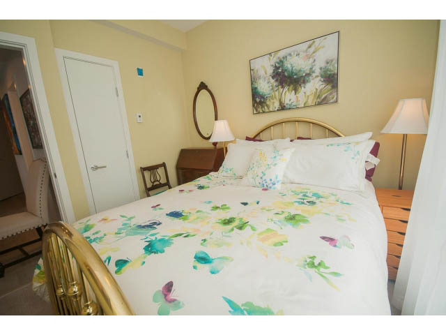 Bright bedroom with floral bedding and wooden headboard, two twin beds, lamps, and artwork on the wall. - 624 - 723 W 3rd St, North Vancouver