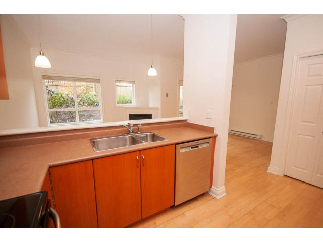 Bright kitchen with wooden cabinets, hardwood floors, and a city view. - 104 - 128 West 21st St, North Vancouver