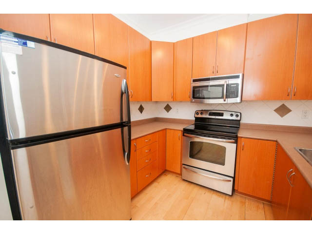 Bright kitchen with stainless steel appliances, hardwood floors, and light wood cabinets. - 104 - 128 West 21st St, North Vancouver