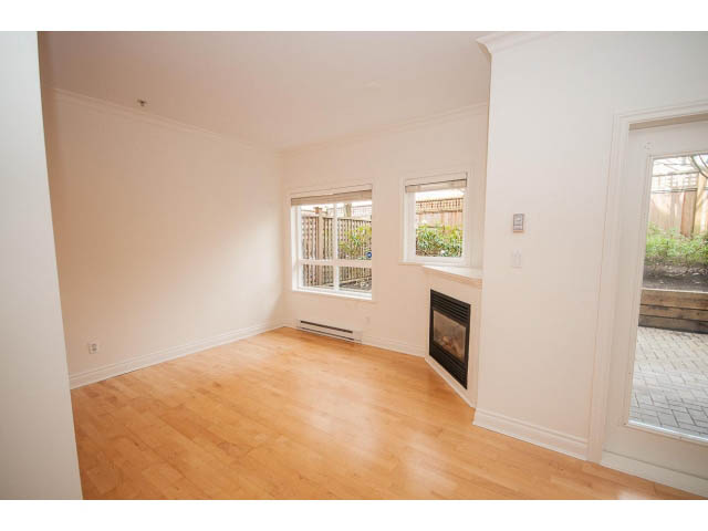Bright living room with hardwood floors and large windows, offering a view of the backyard. - 104 - 128 West 21st St, North Vancouver