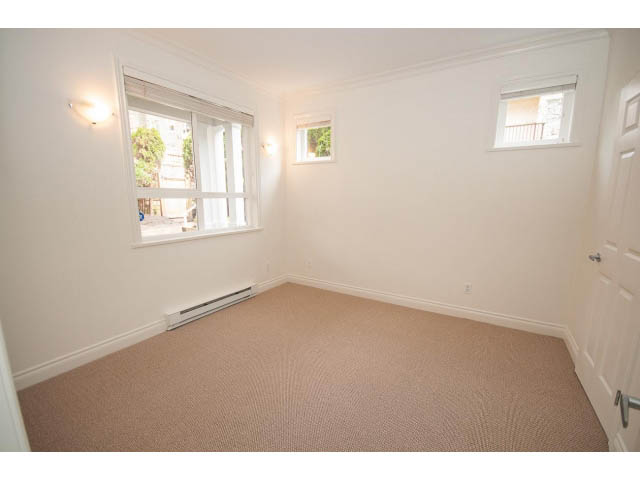 Bright bedroom with carpeted floor and two windows, one with a view of trees. - 104 - 128 West 21st St, North Vancouver