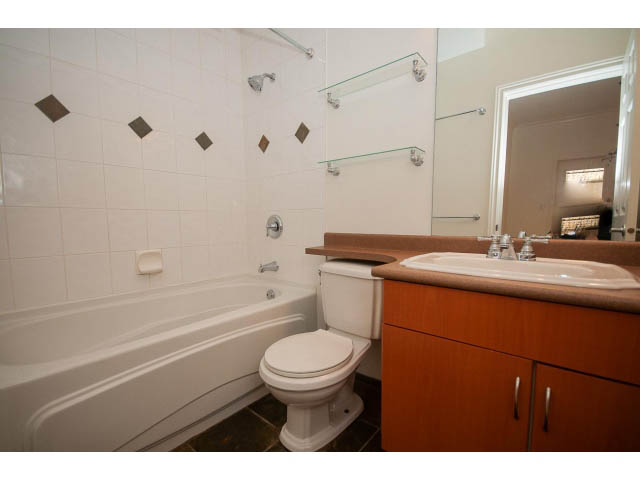 Furnished bathroom with wooden vanity, glass shower, and white bathtub. - 104 - 128 West 21st St, North Vancouver