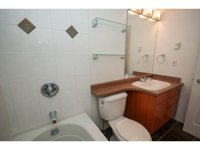 Furnished bathroom with white tiles, wooden vanity, and a bathtub. - 104 - 128 West 21st St, North Vancouver