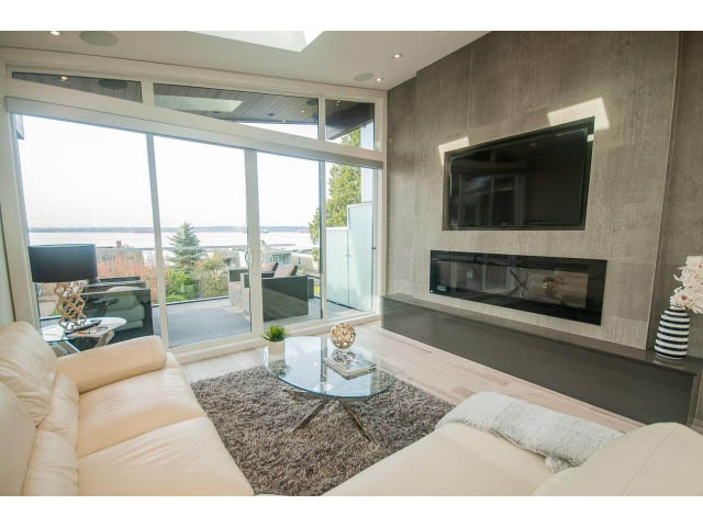 Bright living room with modern fireplace, large windows, and city view. - 2309 Bellevue Ave, West Vancouver