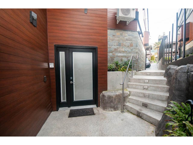 Modern entryway with wooden siding, glass door, and stone steps leading up. - 2309 Bellevue Ave, West Vancouver