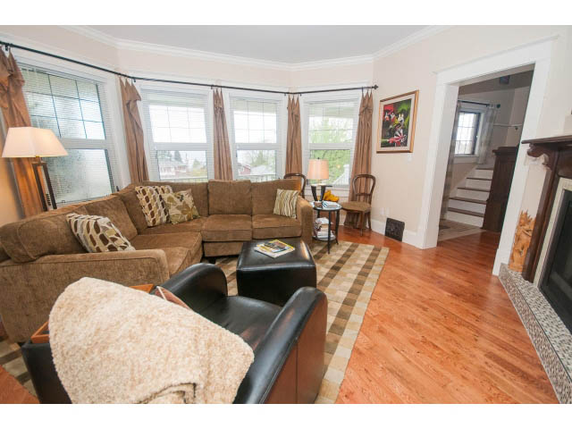 Furnished living room with hardwood floors, bay window, and cozy sectional sofa. - 266 W 6th St, North Vancouver