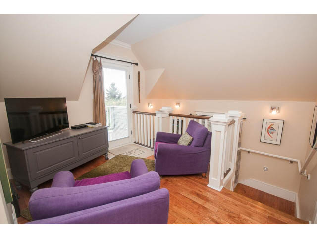 Furnished living room with purple armchairs, hardwood floors, and a flat-screen TV on a gray console. - 266 W 6th St, North Vancouver