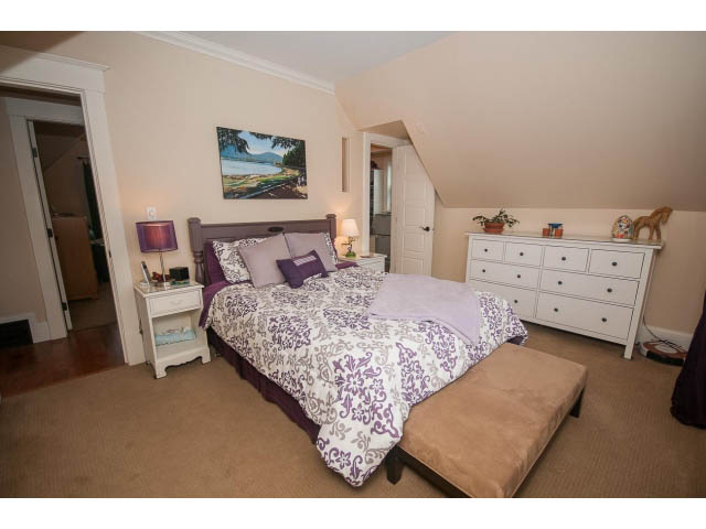 Furnished bedroom with purple and white bedding, wooden dresser, and artwork on the wall. - 266 W 6th St, North Vancouver