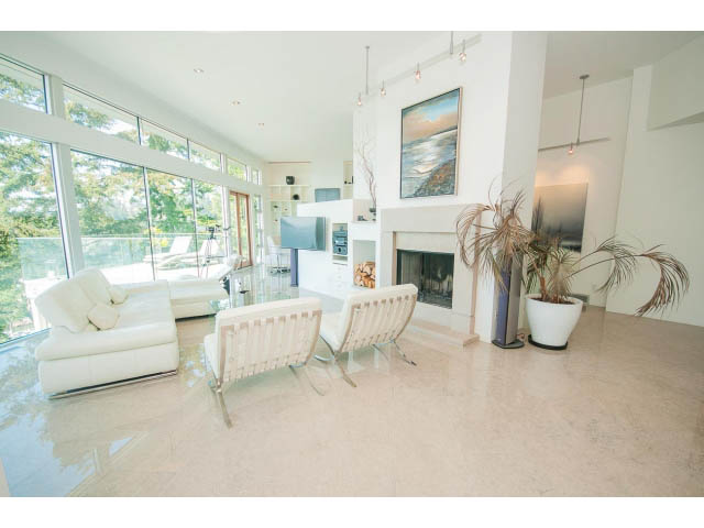 Bright living room with large windows, white furniture, and a fireplace. - 5517 Ocean Place, West Vancouver