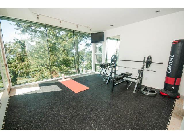 Spacious home gym with large windows, black rubber flooring, and exercise equipment. - 5517 Ocean Place, West Vancouver