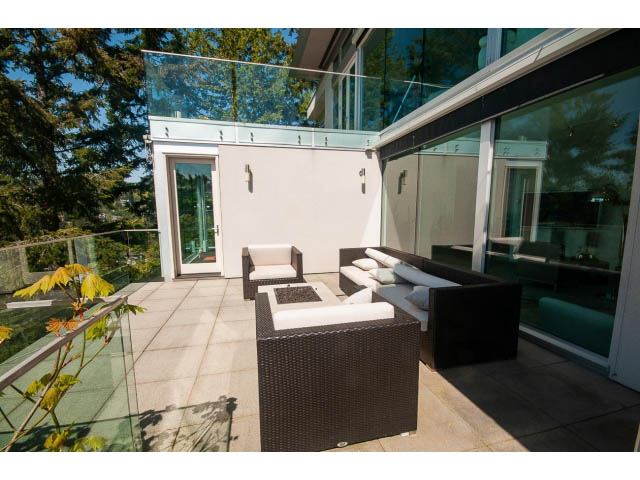 Furnished patio with modern furniture, glass railings, and a fire pit, surrounded by greenery. - 5517 Ocean Place, West Vancouver