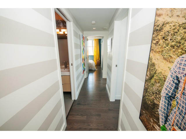 Furnished hallway with striped walls and large artwork, leading to a cozy bedroom with a colorful accent wall.