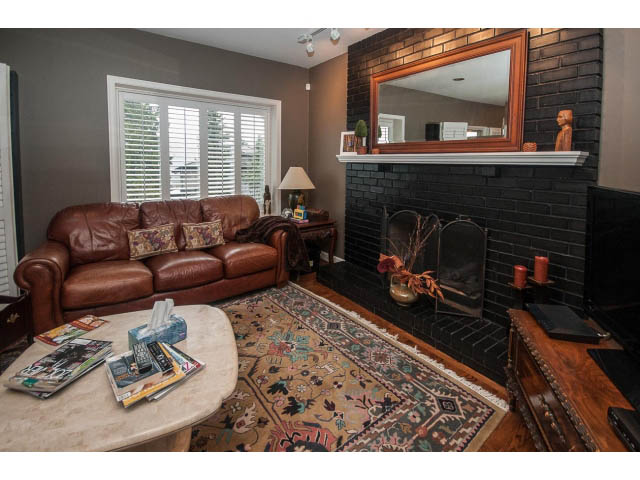 Living room with dark brick fireplace, leather couch, and patterned rug. - Upper - 5237 Timberfeild Road, West Vancouver