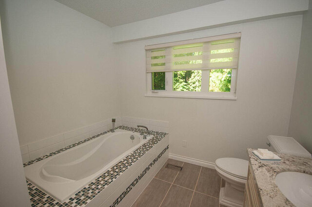 Spacious bathroom with mosaic-tiled tub and granite vanity overlooking greenery. - 5367 Esperanza Drive, North Vancouver