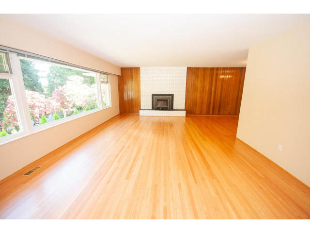Spacious living room with hardwood floors and a fireplace, leading to a bright patio. - 315 Stevens Dr, West Vancouver