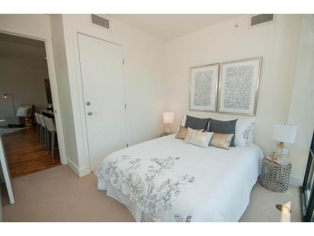 Furnished bedroom with white bedding, wooden floors, and a view of the living area. - 703 - 1863 Alberni Street, Vancouver Downtown