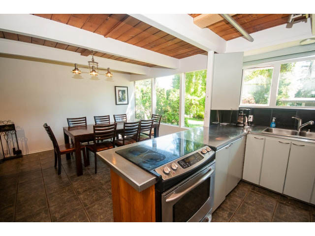 Bright kitchen with stainless steel appliances and wooden beams, open to dining area with large windows. - 640 East Queens Rd, North Vancouver