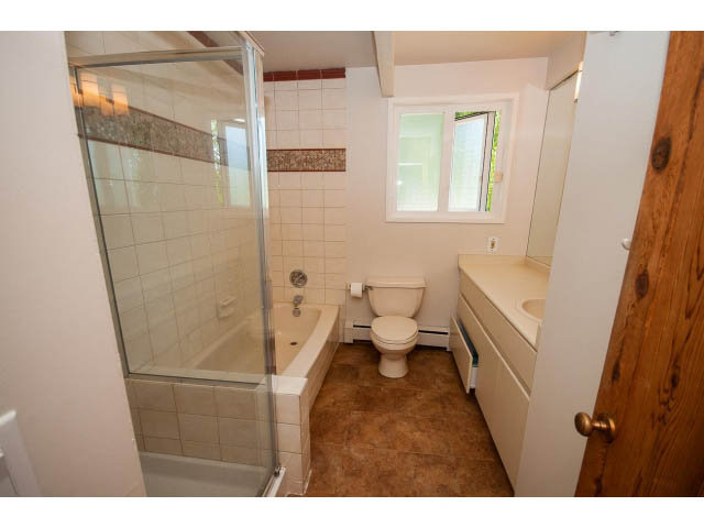 Bathroom with tiled walls, shower, and wooden door. - 640 East Queens Rd, North Vancouver