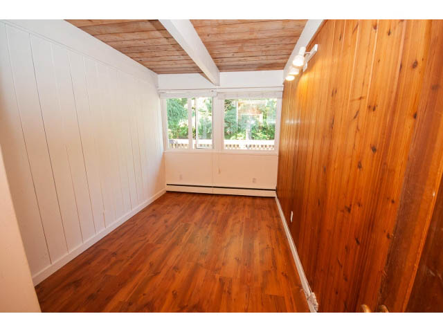 Bright living room with hardwood floors and large windows, offering a view of greenery. - 640 East Queens Rd, North Vancouver