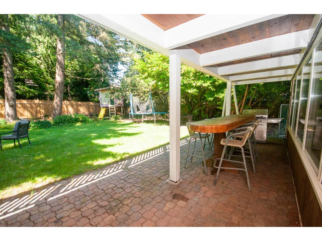 Covered patio with brick flooring and outdoor furniture, surrounded by greenery. - 640 East Queens Rd, North Vancouver