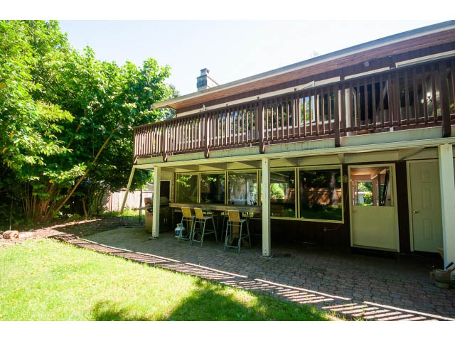Open living area with glass walls, brick patio, and wooden deck. - 640 East Queens Rd, North Vancouver