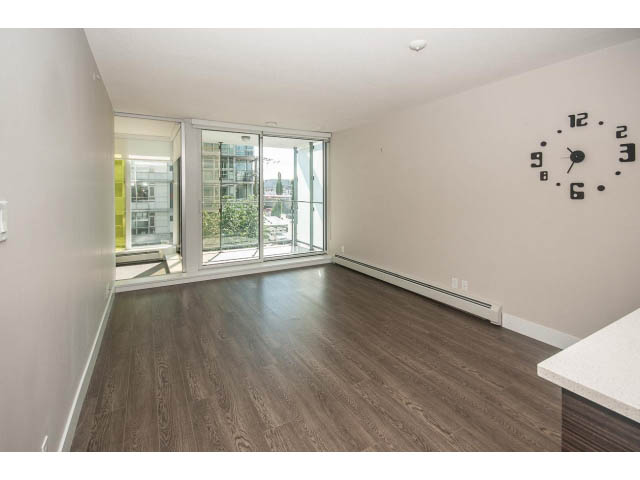Bright living room with hardwood floors, city view, and modern clock on wall. - 301 - 1783 Manitoba St, Vancouver West Side