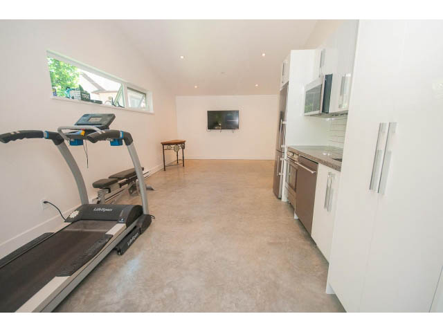 Bright kitchen with white cabinets and stainless steel appliances, open to a living area with a treadmill.