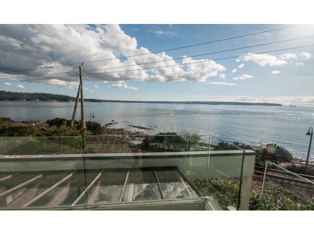 Bright living room with glass railings, waterfront view, and power lines in the background. - 2150 Argyle Ave., West Vancouver