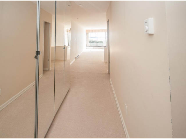 Bright hallway leading to a sunlit living area with carpeted floors and a sliding glass door. - 2150 Argyle Ave., West Vancouver