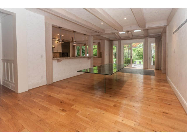 Open-concept living area with hardwood floors and a glass-top table, leading to a kitchen with granite countertops.