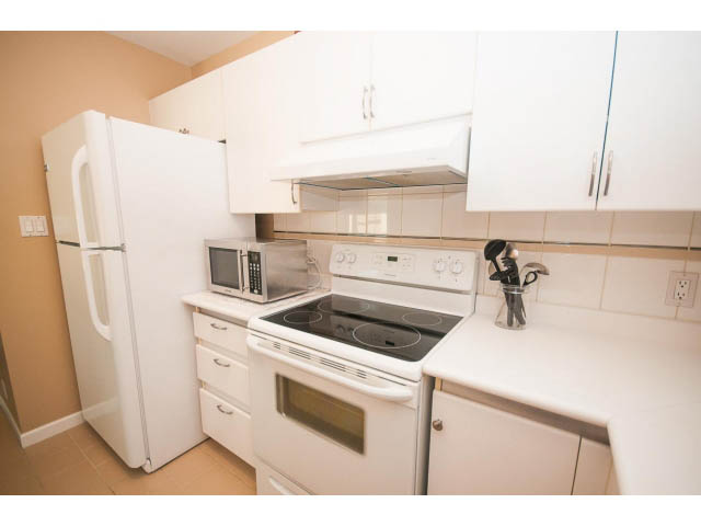 Bright kitchen with white appliances, countertop, and cabinets. - 1213 - 989 Nelson, Vancouver Downtown