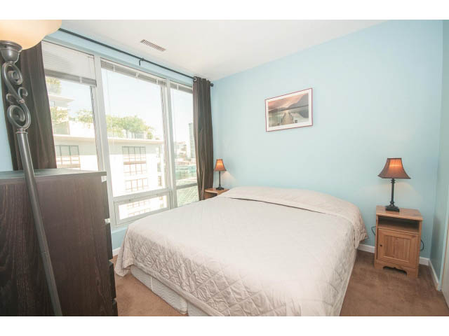 Bright bedroom with city view, furnished, light blue walls, and wooden nightstands. - 1213 - 989 Nelson, Vancouver Downtown