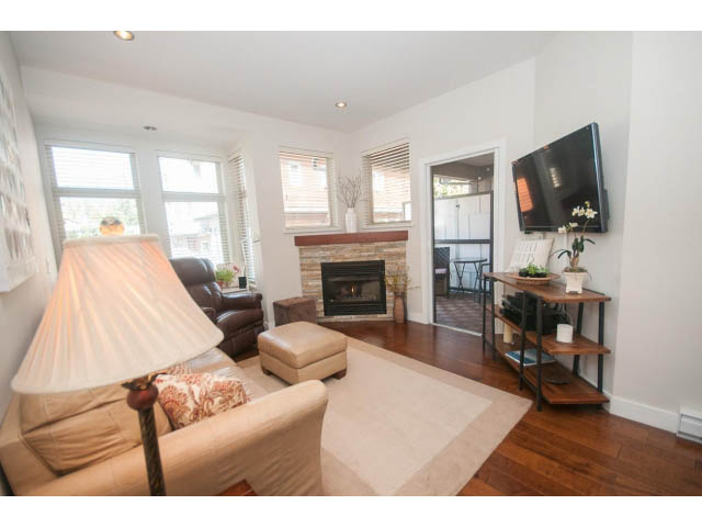 Furnished living room with hardwood floors, large windows, and a cozy fireplace. - 205 - 116 West 23rd, North Vancouver