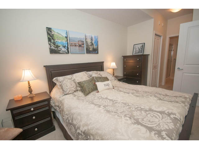 Furnished bedroom with a king-sized bed, patterned bedding, nightstands, and wall art. - 205 - 116 West 23rd, North Vancouver